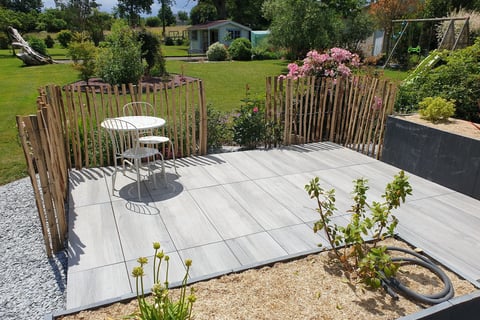 Petite terrasse carrelée avec mobilier de jardin, bordée d'une palissade en bois naturel