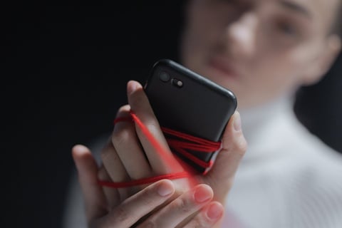 a woman holding a cell phone phone in her hand tied by a red strong. a detox will be necessary.