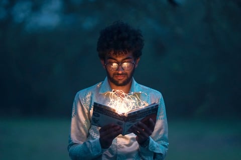 Man reading a book while a yellow glow is seen within it. Reading can help your mental health