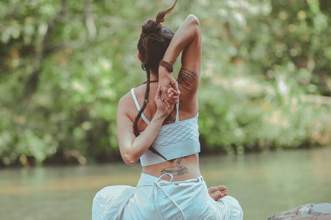 a woman sitting on a rock in a river practicing yoga as she knows her mental health will be boosted
