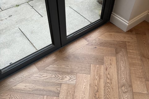 A brown oak herringbone floor with a border against folding doors