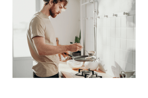 a man in a tan shirt is making pancakes in a kitchen