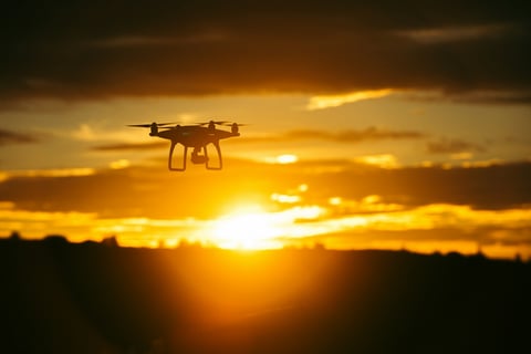 a small drone flying over a sunset