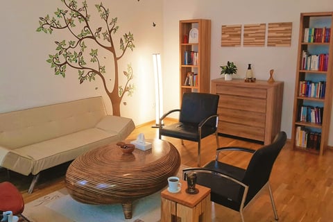 Innenansicht der Praxis: Ein gemütliches Sofa, zwei gemütliche Sessel und Holzmöbel