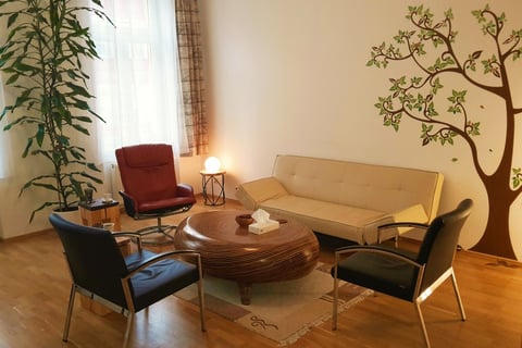 Innenansicht der Praxis: Ein gemütliches Sofa, drei gemütliche Sessel und ein Holztisch