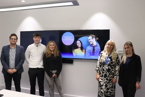 Three apprentices, a sales lead and Tim stand in front of a screen for UK&I apprenticship re-launch.
