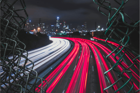 View of freeway at night through broken chainlink fence