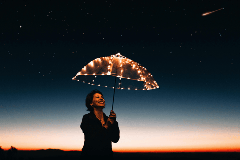 Woman holding lit up umbrella under starry sky with shooting star, she is smiling