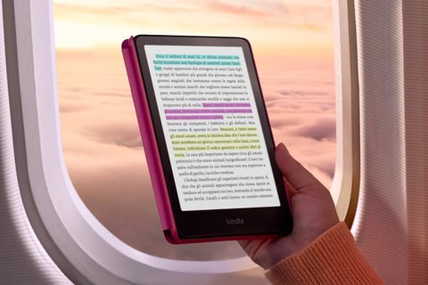Persona leyendo un Kindle dentro de un avión al atardecer, destacando la portabilidad y comodidad de