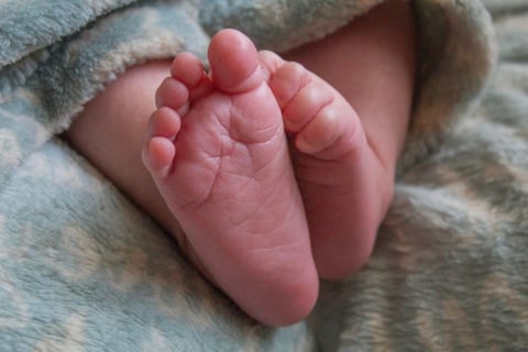 Close-up of a baby's toes peeking out from a soft blue blanket, with one foot's toes gently curled inward.