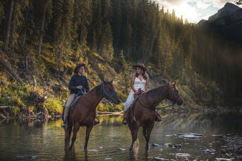 two people riding horses in the water in Banff