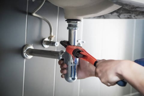 man using a mini pipe wrench to turn a pipe under a sink