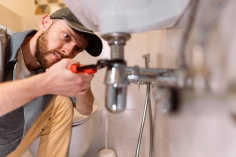 plumber focusing very hard while he is turning a pipe under a sinkj