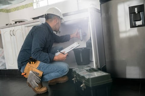 plumber inspecting a pipe under a sink wearing a hard hat