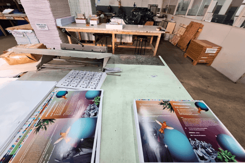 Impressos offset recém-saídos na mesa de corte da Editograf com pilhas de papel ao fundo.