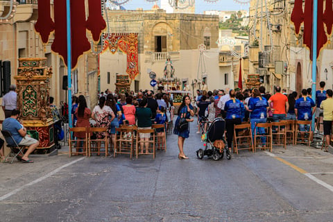 People sitting in a narrow street in front of a statue of St Mary.