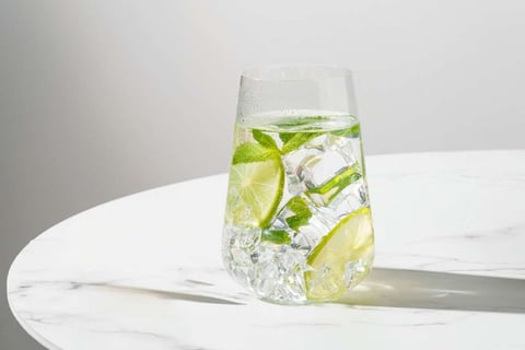 Copo de água com limão sobre mesa iluminada pela manhã