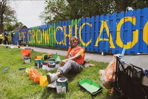 Painter sitting in front of mural with paint cans