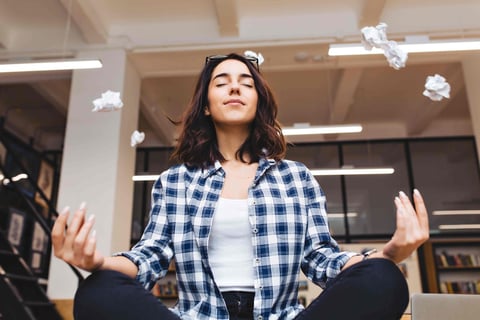 Relaxing time joyful young woman having meditation on table in office surround flying papers.