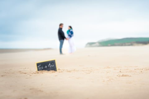 Un couple sur une plage de sable blanc face à face avec une ardoise au premier plan