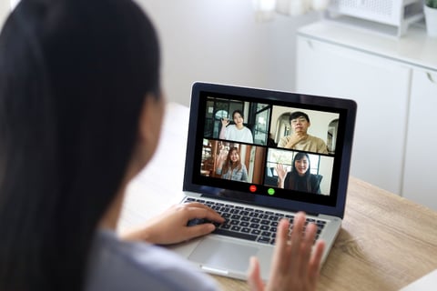 a woman sitting at a table with a laptop computer screen showing a video call