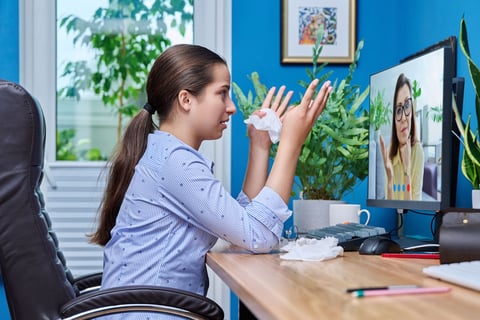 a woman sitting at a desk with a computer screen showing a video chat