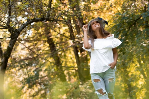 a woman in ripped jeans and a white top walking in the woods