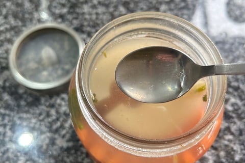 a spoon over a jar taking out a little brine