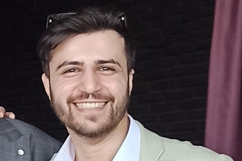 Adem Asha in a suit and tie smiling for the camera