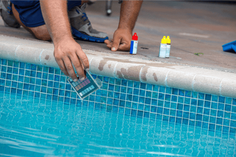 Close-up image of a pool tech kneeling on the edge of a pool performing water testing and balancing