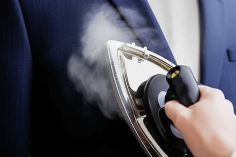 An iron steaming a dark blue suit jacket.