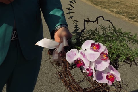 Aranjament cu orhidee, verdeață și ramuri, ținut în mână.