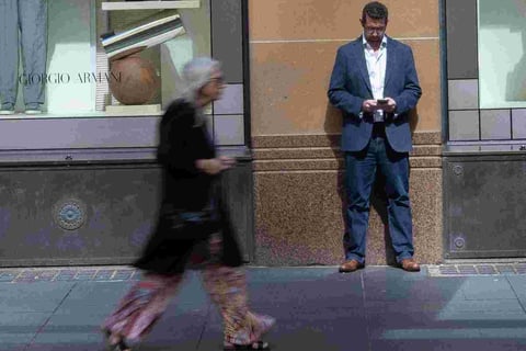 Man standing motionless against wall while blurred woman passes in front of him