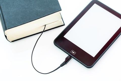 An iPad is connected to a hardbound book with USB cable from the iPad to the hardbound book. 