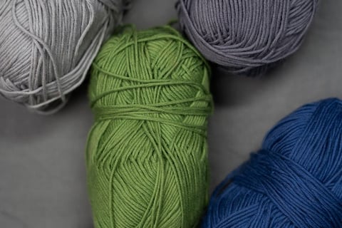 Colorful skeins of yarn in gray, green, blue, and white tones arranged on a neutral fabric backgroun