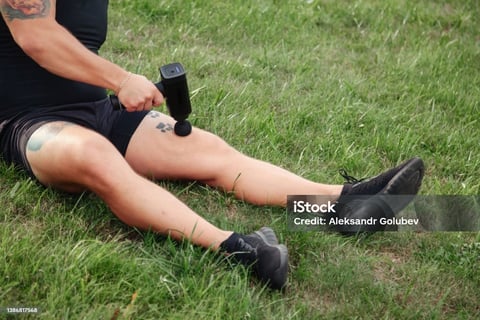 a man with tattoos on his leg using massage gun