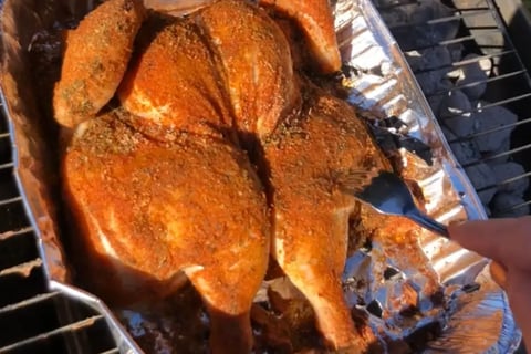 Spatchcocked whole chicken coated in homemade Cajun seasoning on charcoal grill