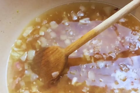 broth being stirred in dutch oven with onions garlic and smoked meat for southern cabbage recipe with smoked ham