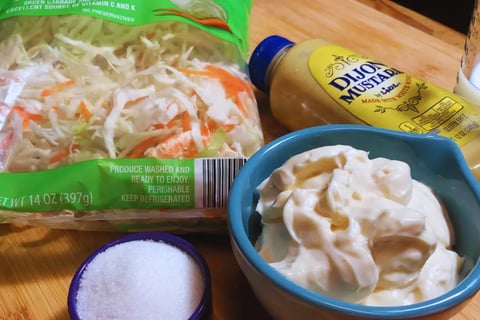 Coleslaw ingredients arranged on a wooden cutting board, including cabbage, carrots, and seasoning items