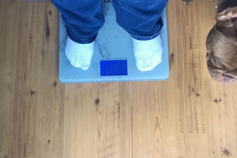 Everyday Dana on a weight scale with her dog beside her.