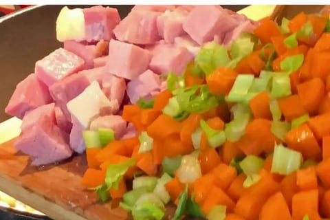 Cubed ham with chopped carrots and celery on a cutting board by the pot