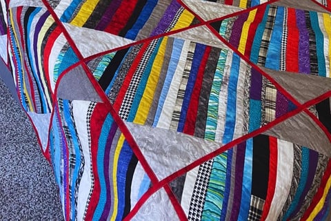 colorful quilt with red sashes and multicolored strips made for my son