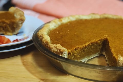 Two harvest pies on a table—one whole with a slice missing and another showing a single slice of sweet potato and pumpkin pie