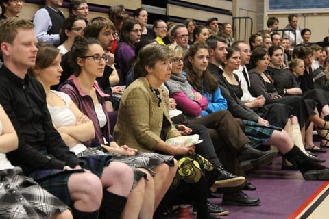 Crowd of people sitting on bleachers, some in kilts, intently watching something