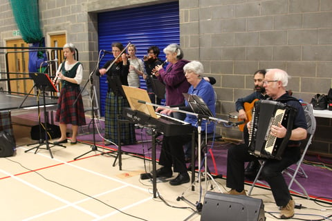 Musicians practicing next to a stage in a gymnasium 