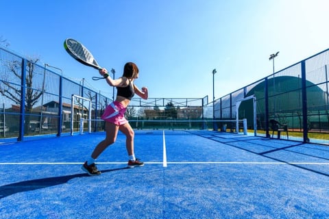 a woman in a pink skirt playing Padel outdoors