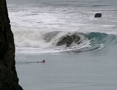 A bodyboarder riding a wave and another surfer watching from the water