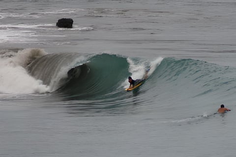 A bodyboarder riding a wave and another surfer watching from the water