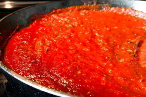 a pan of red sauce with a wooden spoon