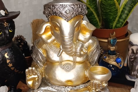 La foto muestra una figura decorativa de Ganesha en colores plata y oro